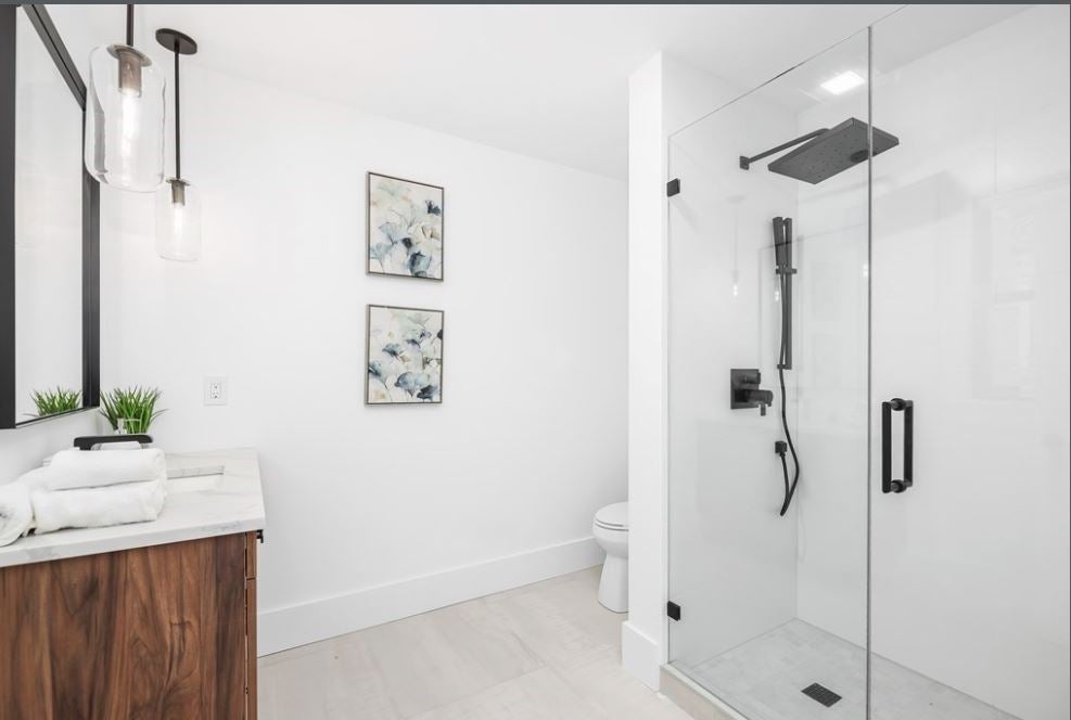 A bathroom with a walk-in shower that has multiple heads. All the fixtures are black. The bath also has a single floating vanity. The toilet is tucked in a corner behind the shower.