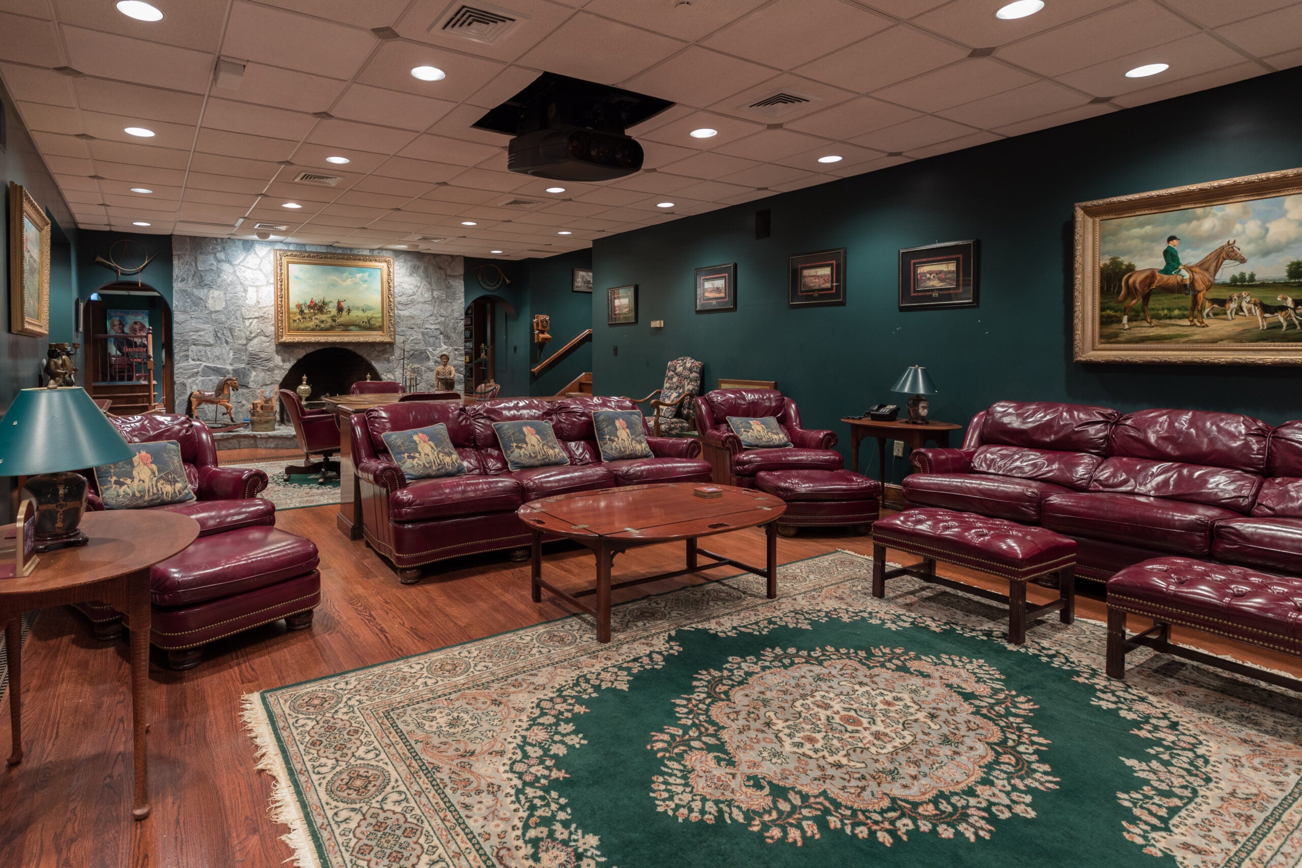 A screening room with red leather recliners, dark green walls, a projector hanging from the ceiling, and a stone fireplace.