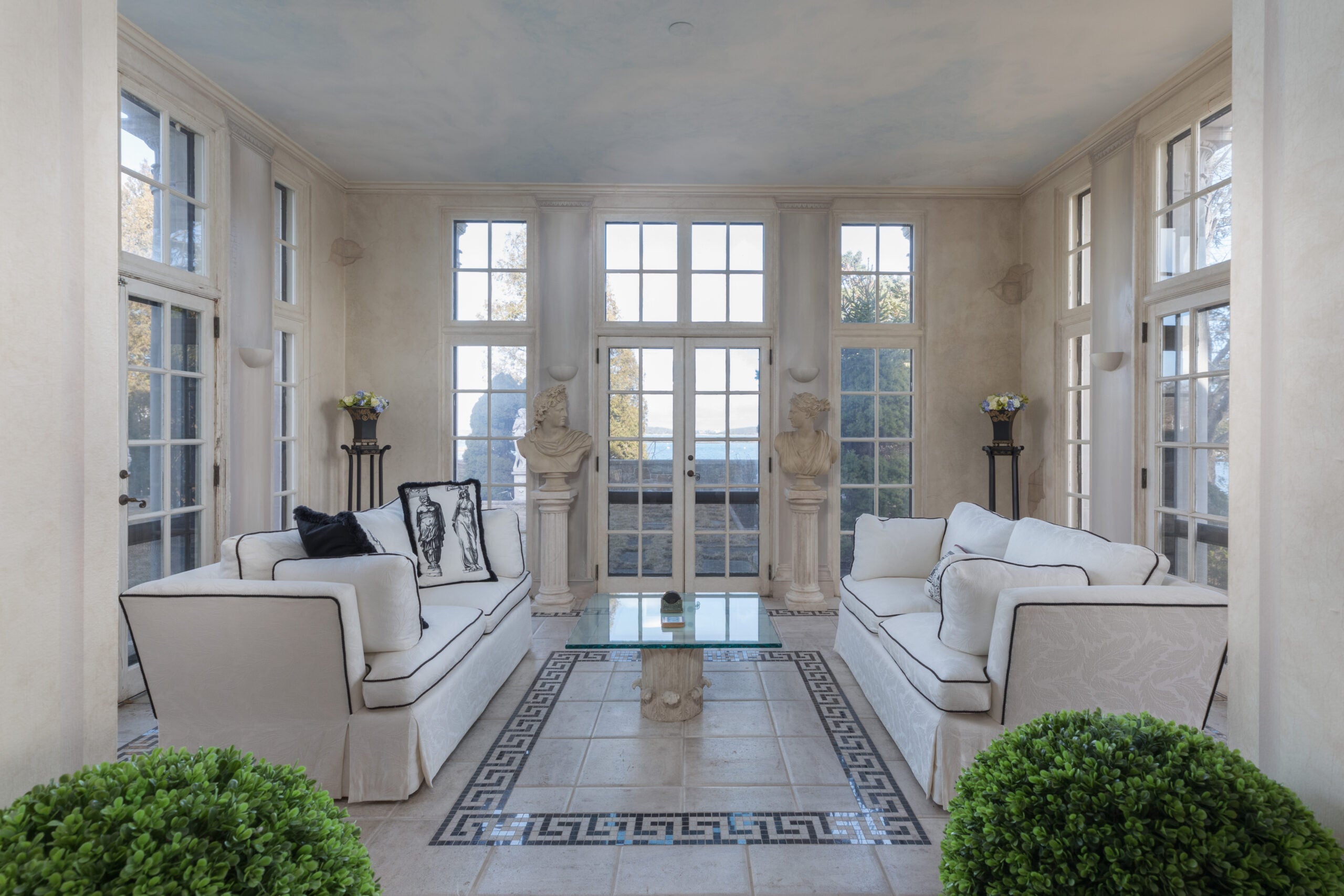 A sunroom in a Cohasset estate with an tile floor inlay, French doors, and two white couches sitting opposite each other with dark piping.