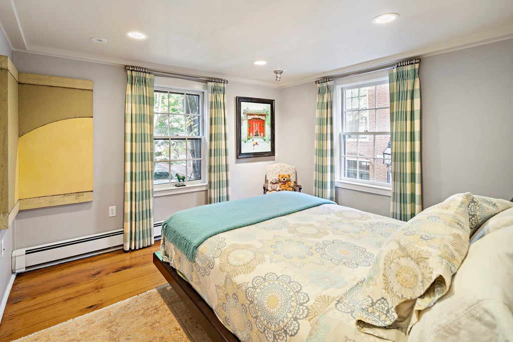 A room with wood flooring, green buffalo-check drapes, and a floral bedspread. The walls are gray.