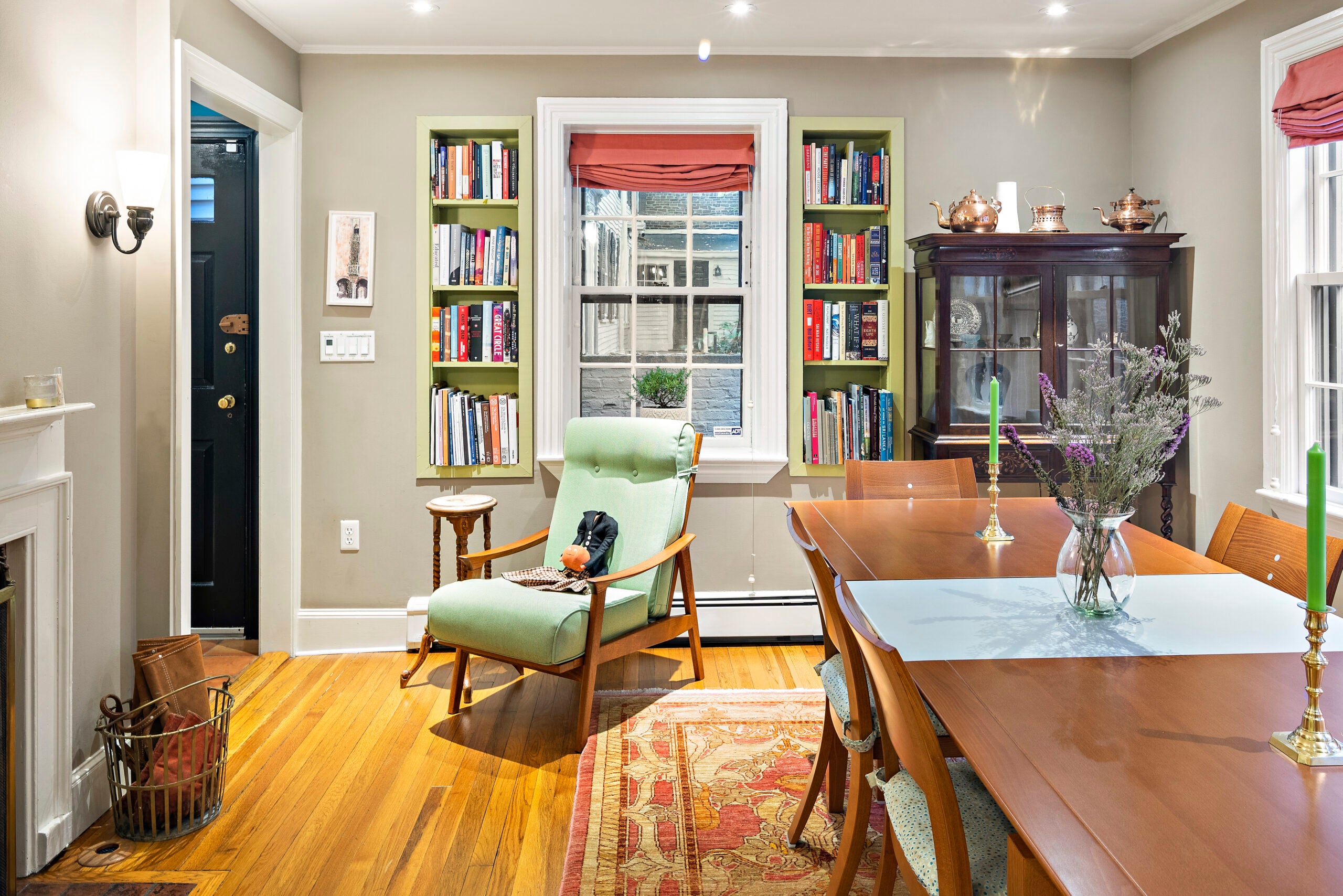 A room with built-in bookshelves, wood flooring, a long wood table, and tan walls. The window has a dark rose roll shade.