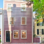 A wood-clad, pink multi-story home with a black door and no shutters.