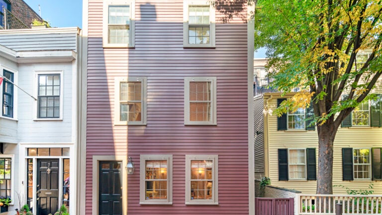 A wood-clad, pink multi-story home with a black door and no shutters.