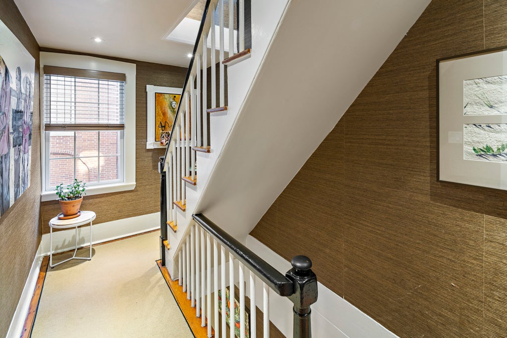 A view of two stairways with black banisters, white balusters, and walls clad in brown grass-cloth wallpaper.