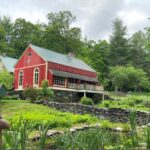 An old home on the market with a red barn and a pond.