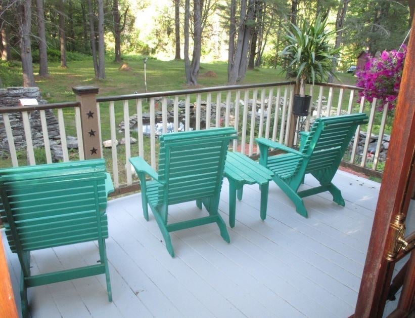 Aqua chaises sit on a gray deck overlooking a pond and woods.