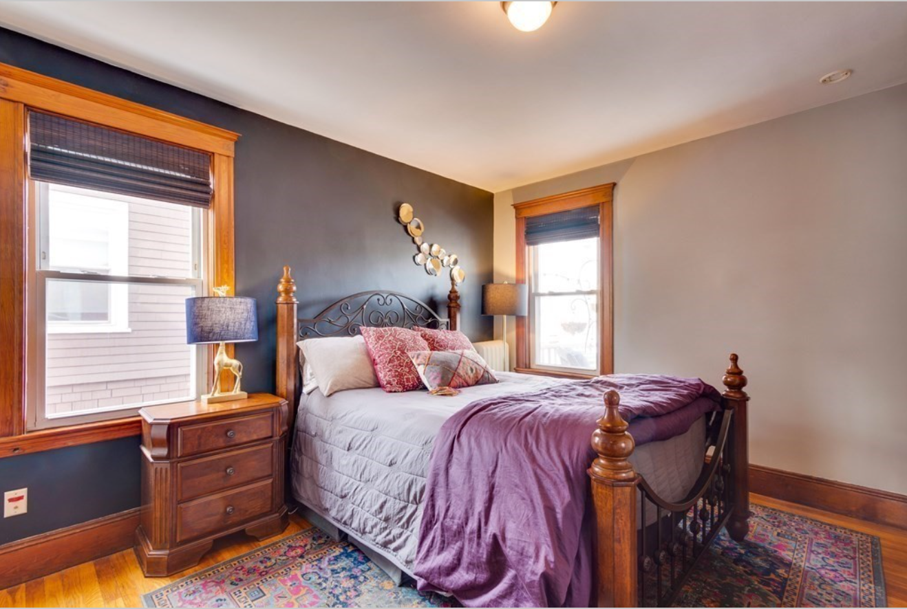 The primary bedroom has two single-hung windows and an eggplant-colored accent wall.