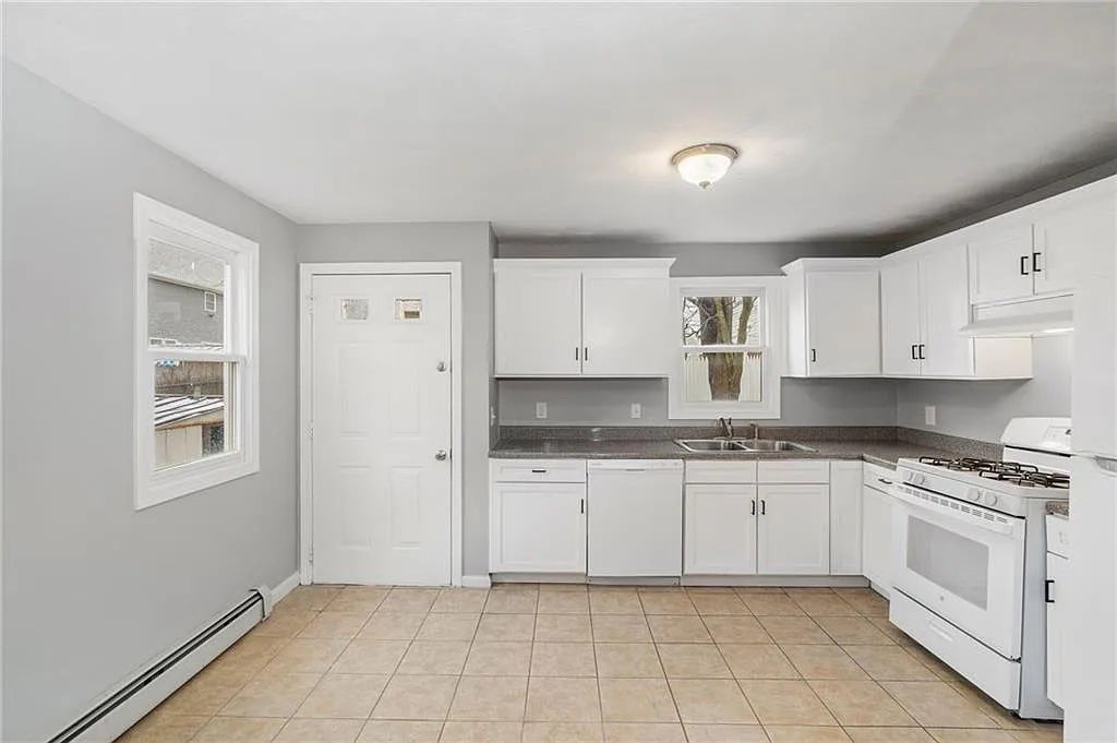 The kitchen has white cabinetry, two single-hung windows, and tiled floors.