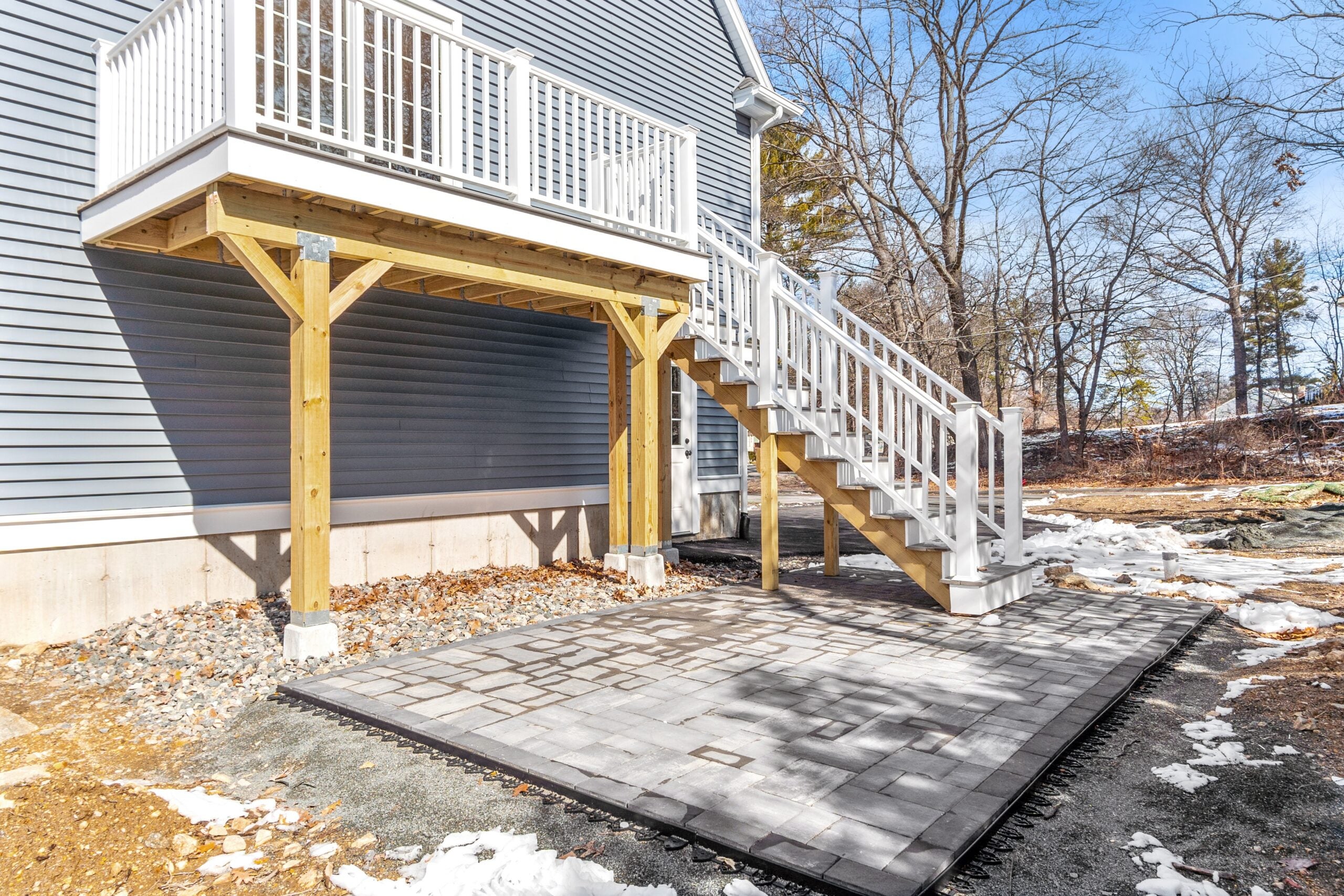 A view of a deick with white railings and a gray paver patio.