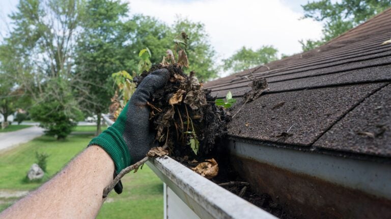 A man clearing the gunk out of a home's gutters to illustrate how to get ready for spring