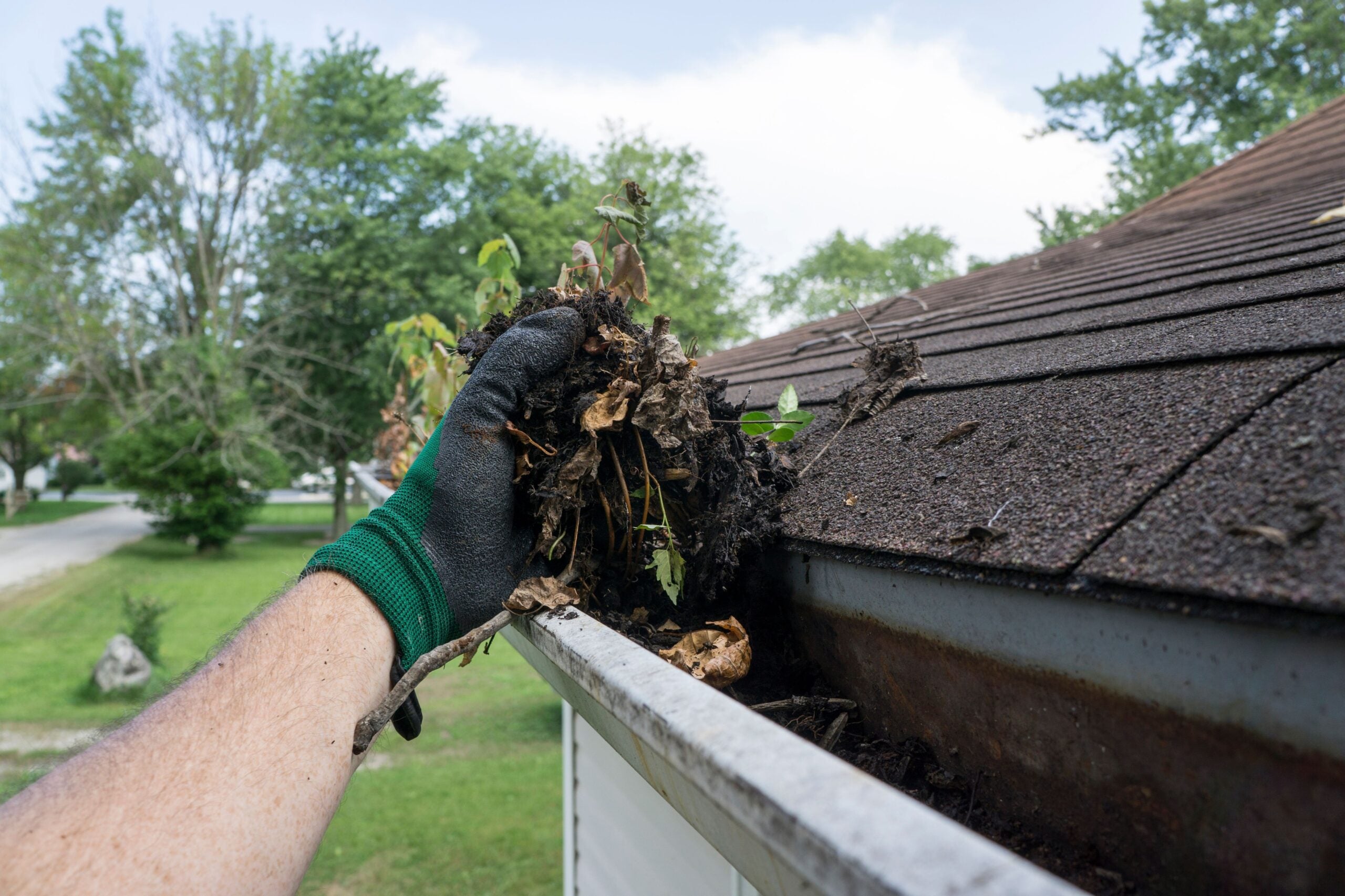 A man clearing the gunk out of a home's gutters to illustrate how to get ready for spring