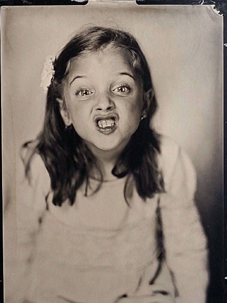 A black-and-white candid tintype image of a young girl, making a funny face for the camera.