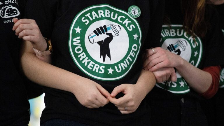 Starbucks employees are seen wearing black T-shirts with a green, white, and black logo resembling Starbucks', showing a raised first with the words "Starbucks Workers United."