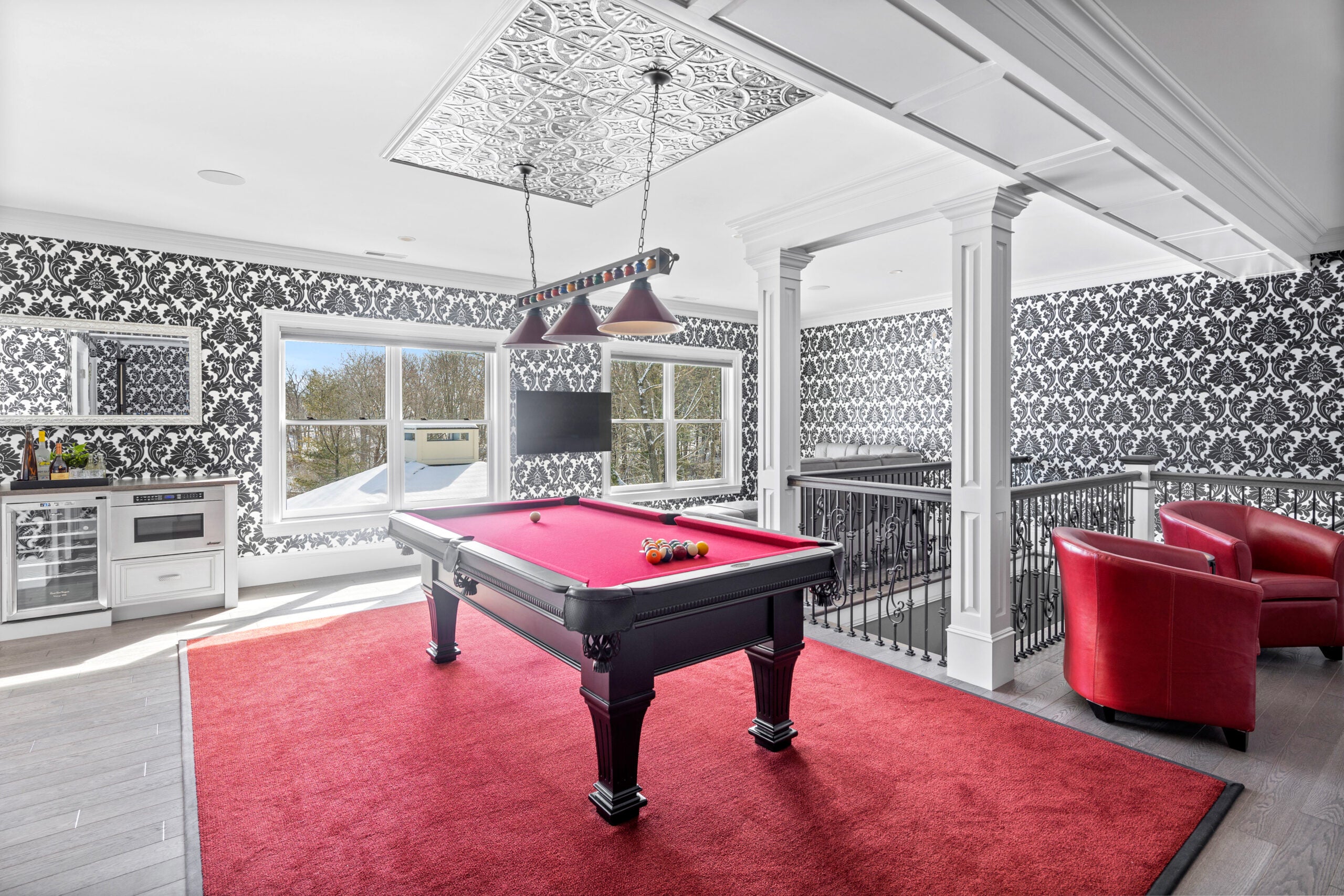 The billiards room and home movie theater are both upstairs. The billiards room has plush red carpeting and black and white wallpapered walls.
