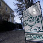 A real estate sign in front of a yellow Colonial shows the property during wintertime. Buyers are facing a high average mortgage rate.