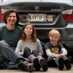 Peter Starostecki and his kids Sadie, center, and Jo Jo, pose behind their car with the vanity license plate that the state of Maine has deemed in appropriate,