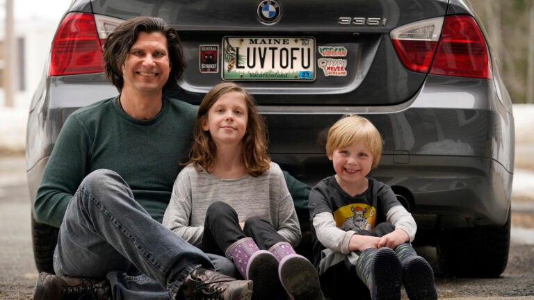 Peter Starostecki and his kids Sadie, center, and Jo Jo, pose behind their car with the vanity license plate that the state of Maine has deemed in appropriate,