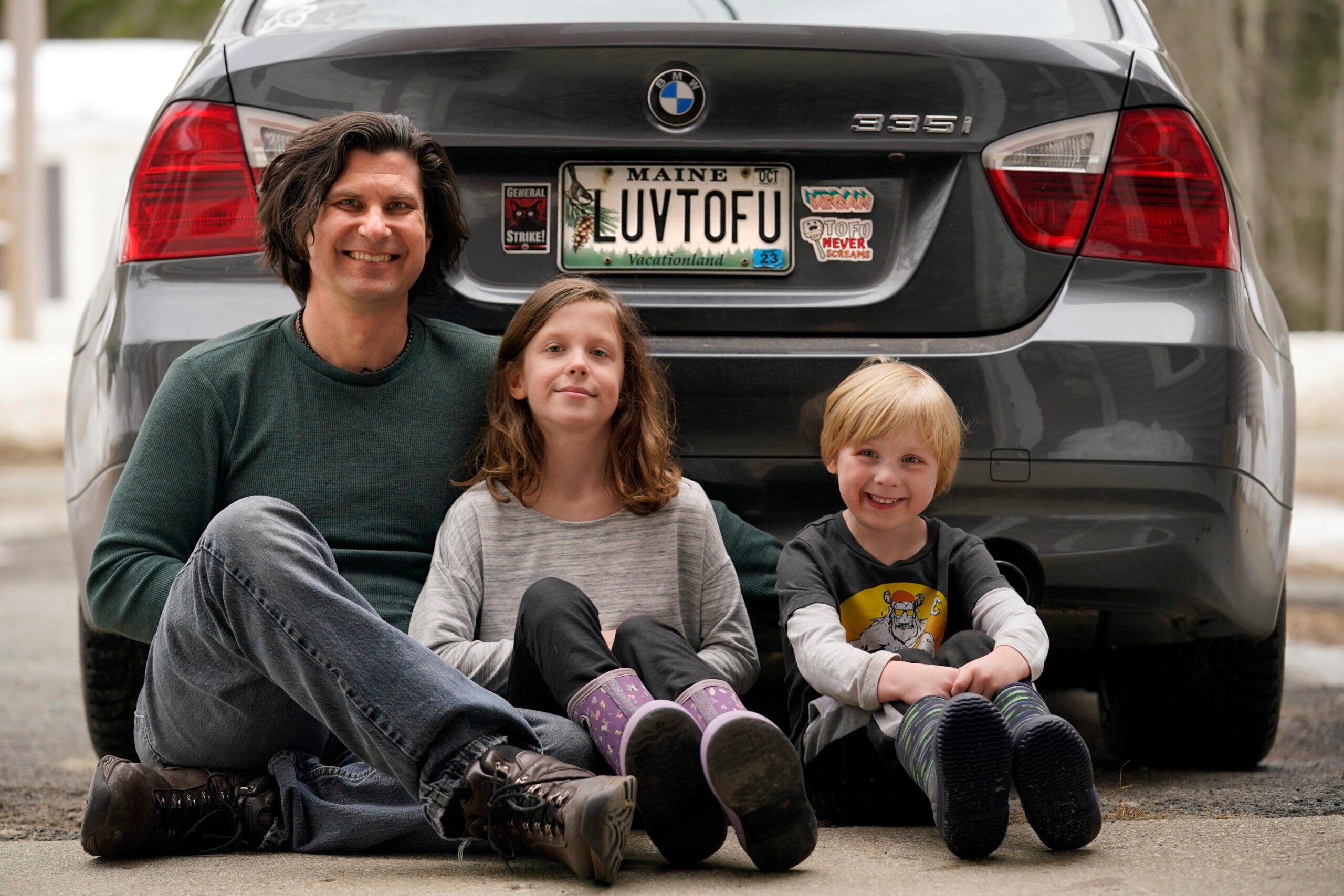 Peter Starostecki and his kids Sadie, center, and Jo Jo, pose behind their car with the vanity license plate that the state of Maine has deemed in appropriate,