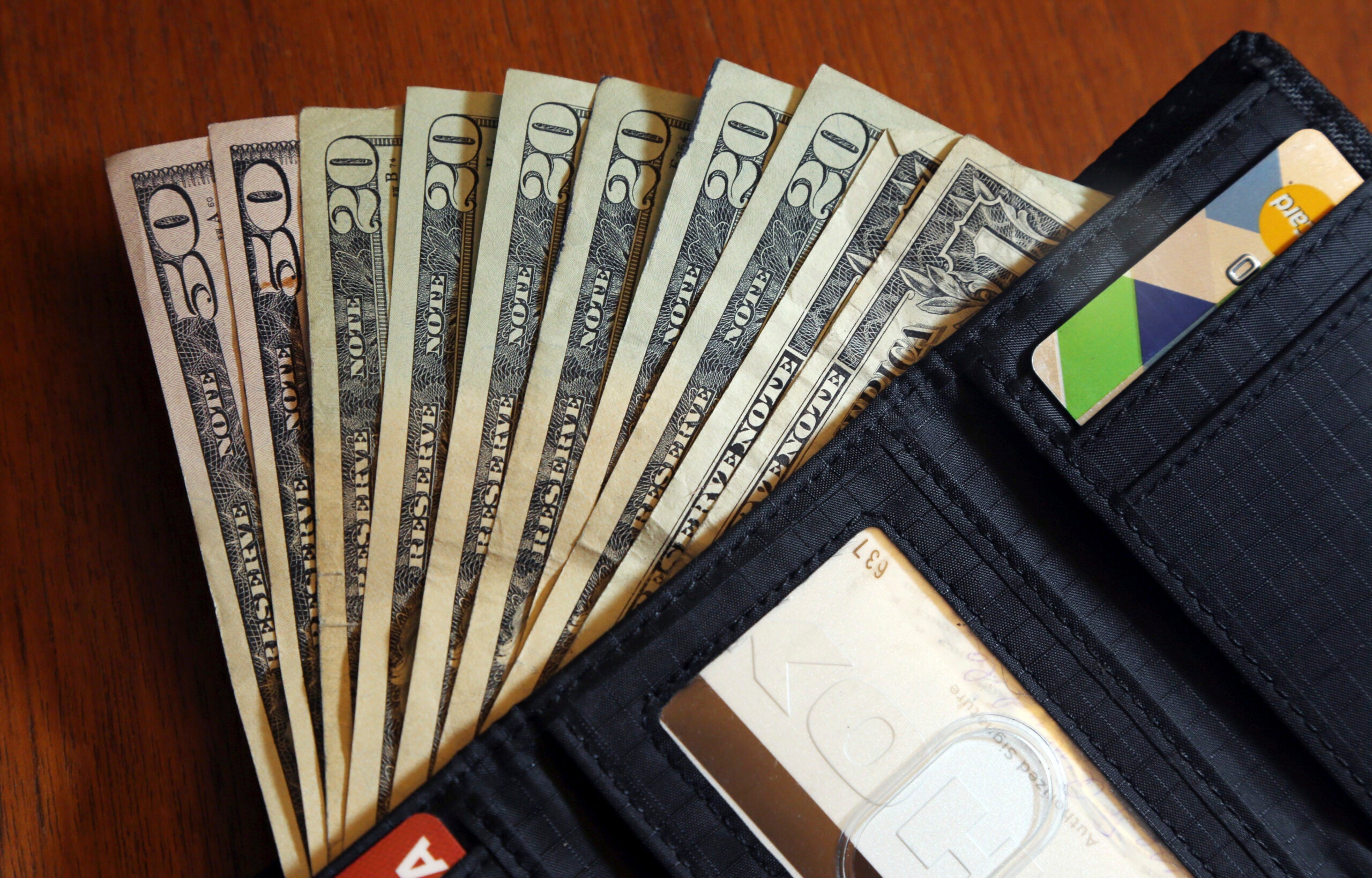 $50, $20, and $1 bills are fanned out from an open black wallet.