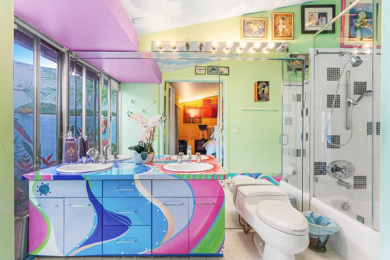 One of the four bathrooms features blue, purple, pink, and green cabinetry, a shower-tub combo, and a double vanity with floor-to-ceiling mirror.