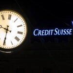The illuminated logo of Swiss bank Credit Suisse is seen behind a clock