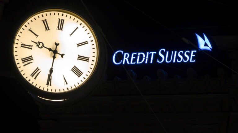 The illuminated logo of Swiss bank Credit Suisse is seen behind a clock