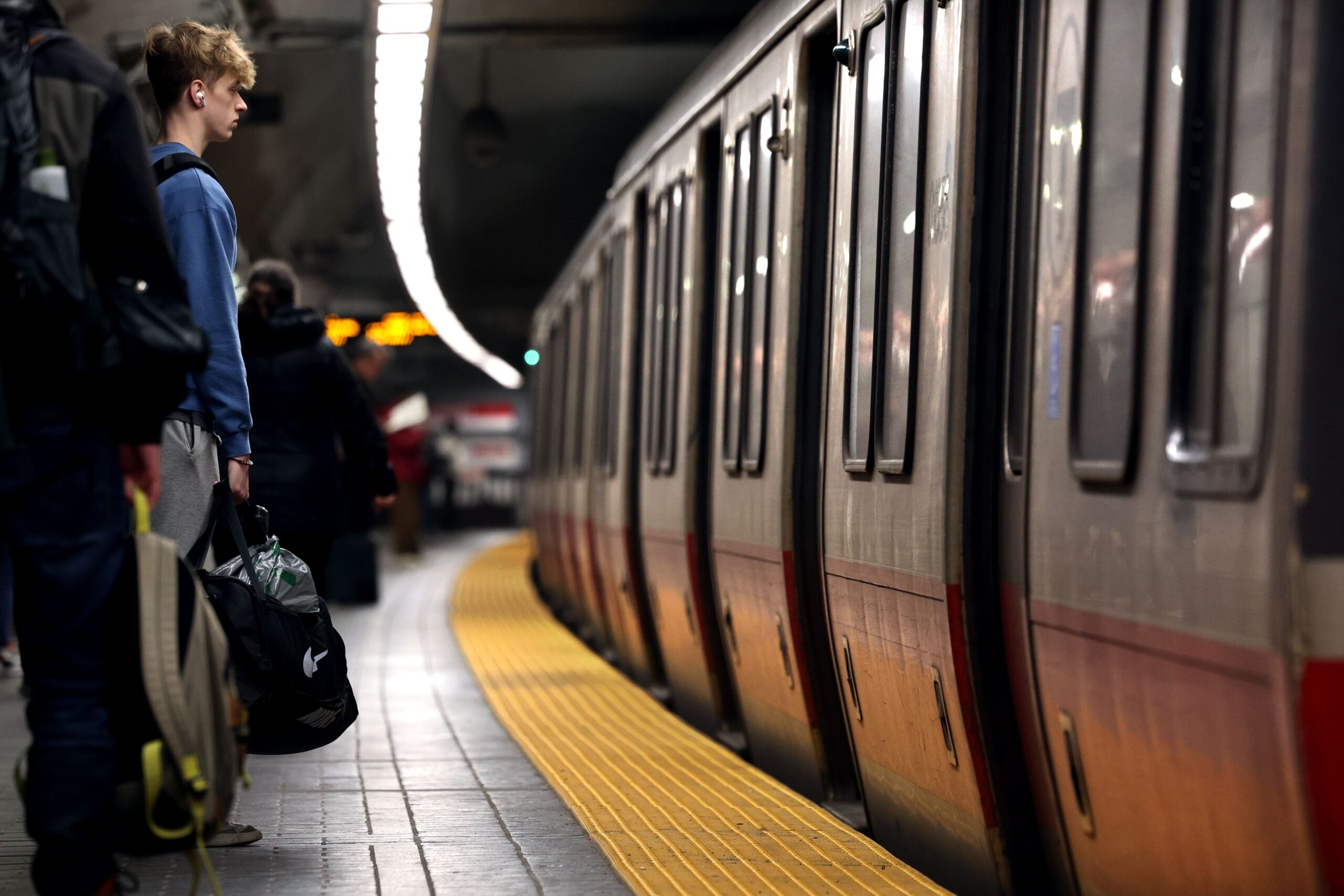 A Red Line MBTA train arrives at Park Street as passengers look on from behind the yellow safety strip.
