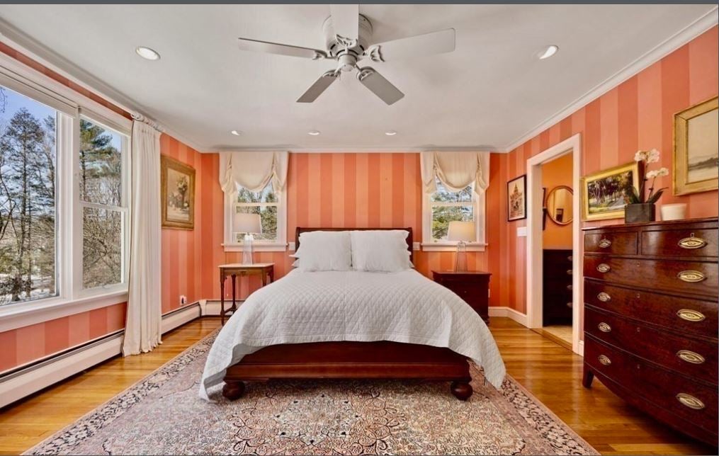 A bedroom with hardwood flooring, white bedding, two windows, and orange-striped wallpaper for a bold interior design.