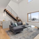 A view of a condo for sale with white walls, big windows, and a cantilevered staircase.