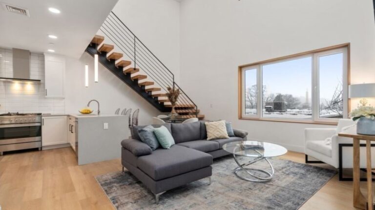 A view of a condo for sale with white walls, big windows, and a cantilevered staircase.