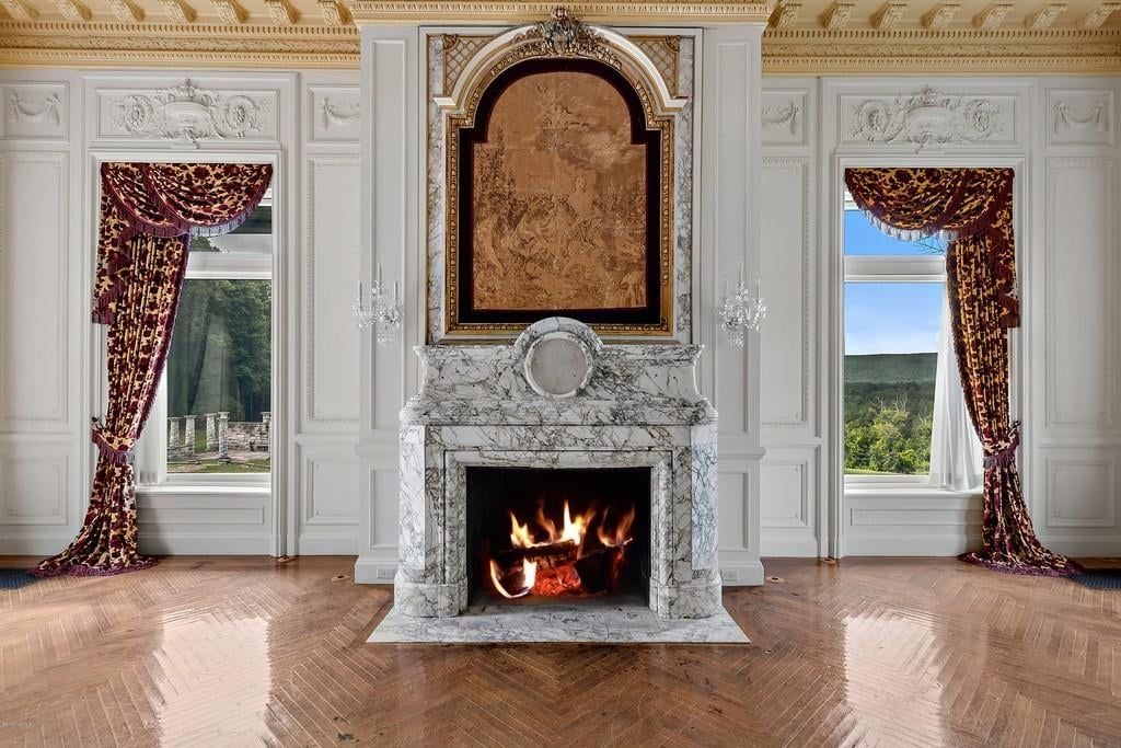 A marble fireplace in a grand room of a Berkshires mansion with crown and picture frame molding. The flooring is herringbone.