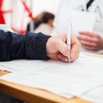 A person signs a document on a clipboard