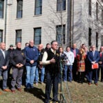 International Association of Firefighters General President, Edward Kelly, stands in front of a group of IAFF representatives in front of a white building