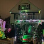 Chris and Daisy Hugenberger's Roslindale home, decorated with green and white holiday lights, a shamrock arch, and an inflatable dinosaur wearing a shamrock hat and holding a mug of beer.