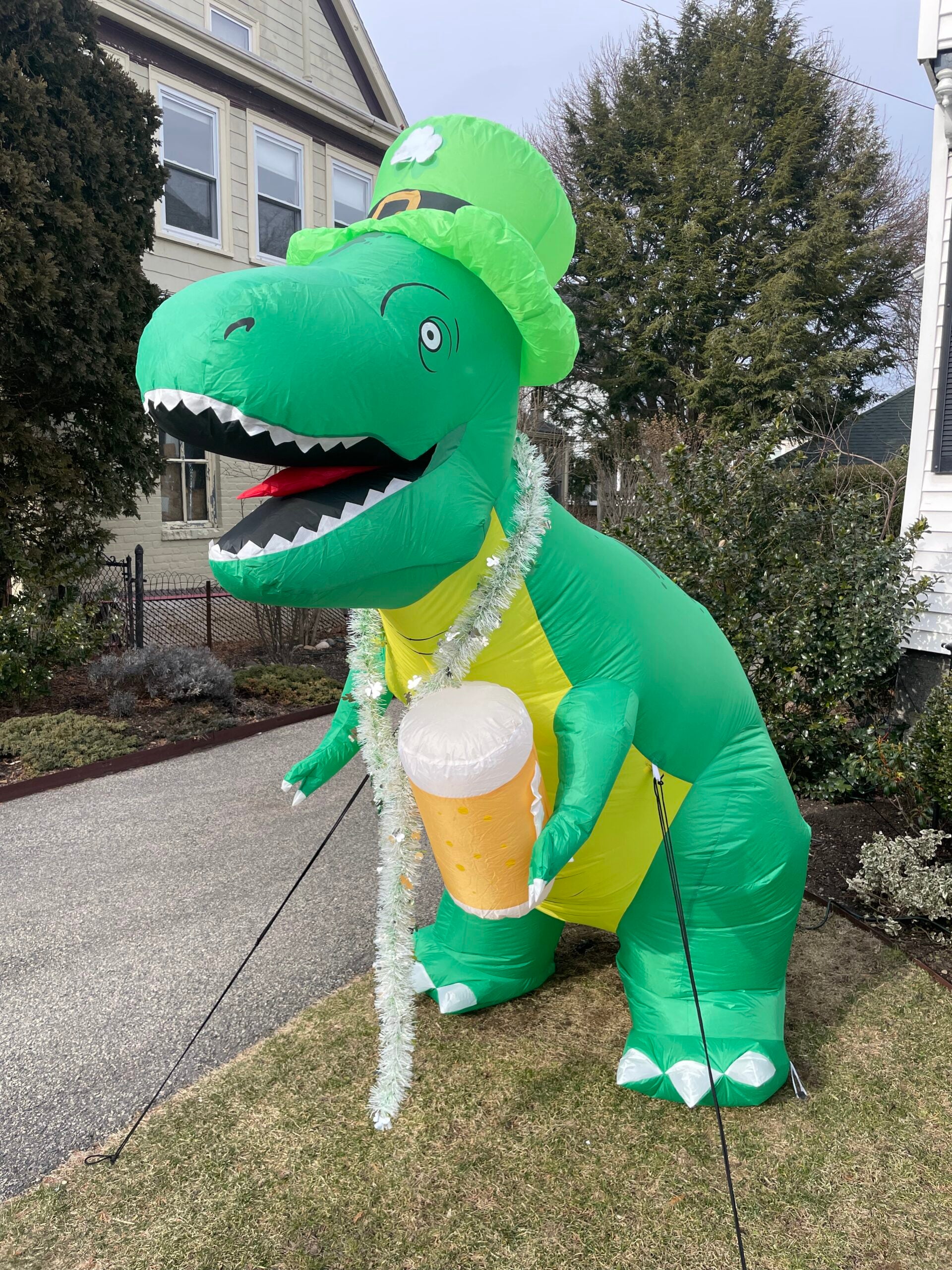 An inflatable dinosaur wearing a shamrock hat and holding a mug of beer.