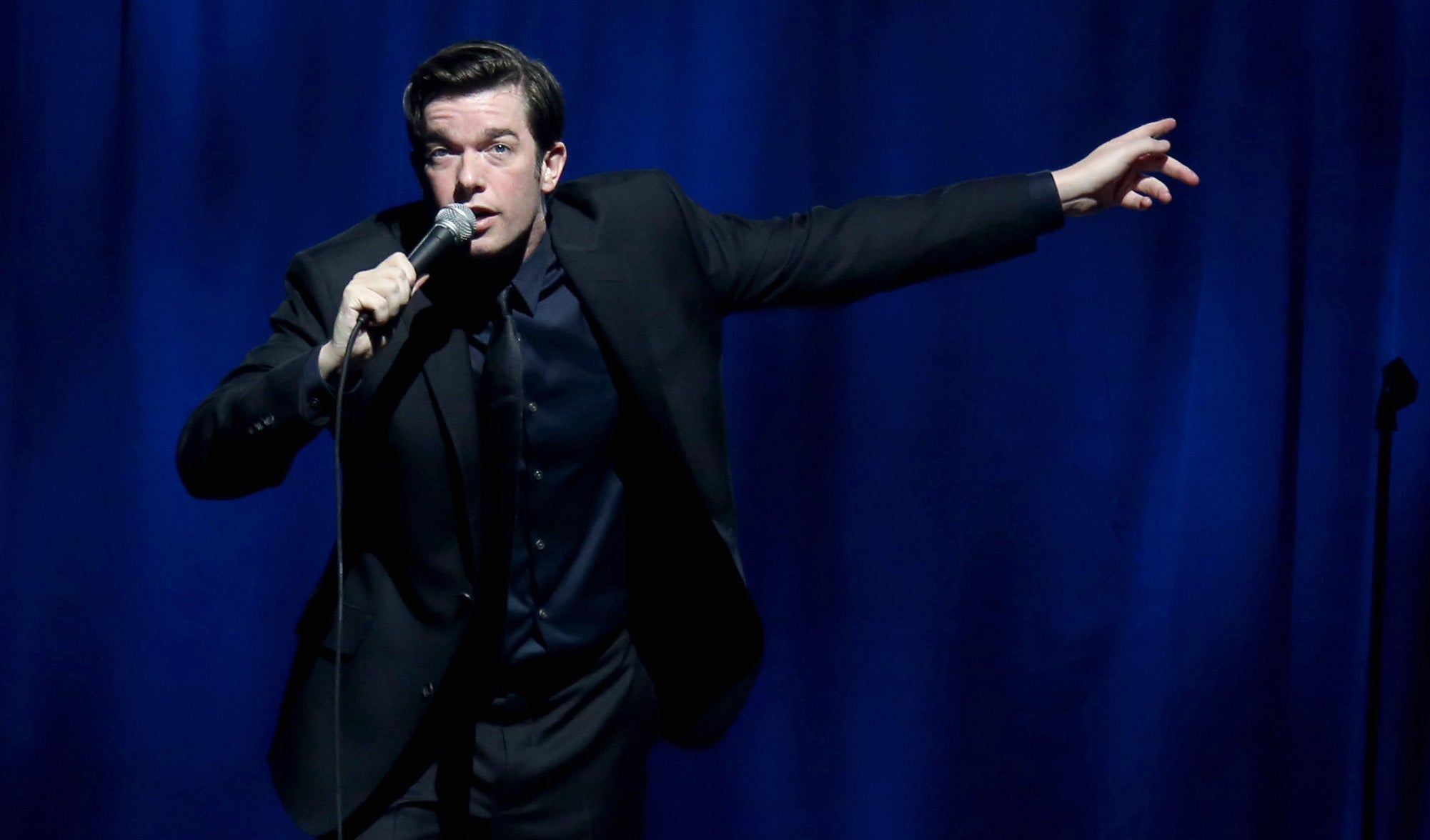 John Mulaney gesticulates while performing comedy.