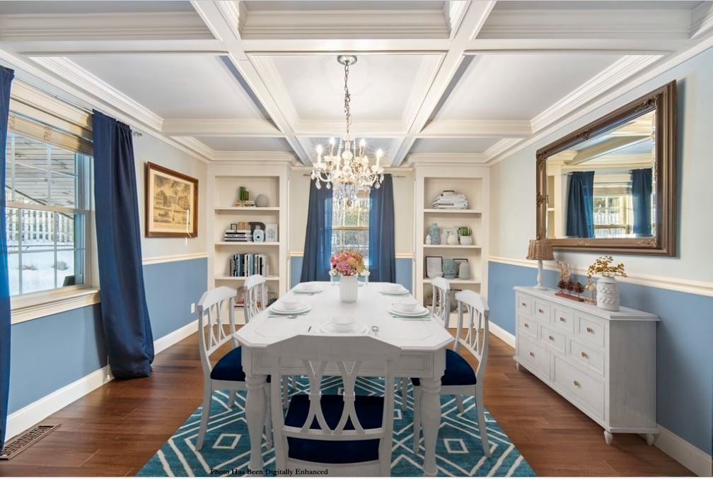 A dining room with a white coffered ceiling, built-in bookcases, long blue curtains, and white walls above the chair rail and blue walls beneath.
