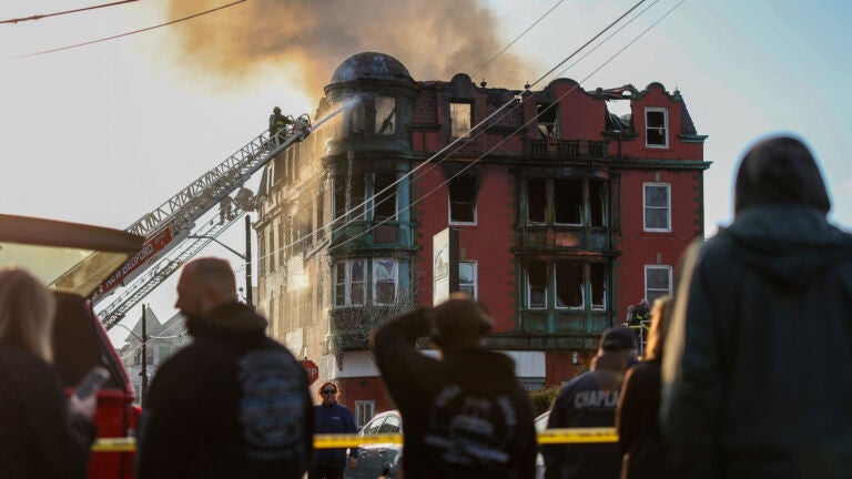 Several people look at the Royal Crown Lodging, a New Bedford rooming house that erupted in flames.