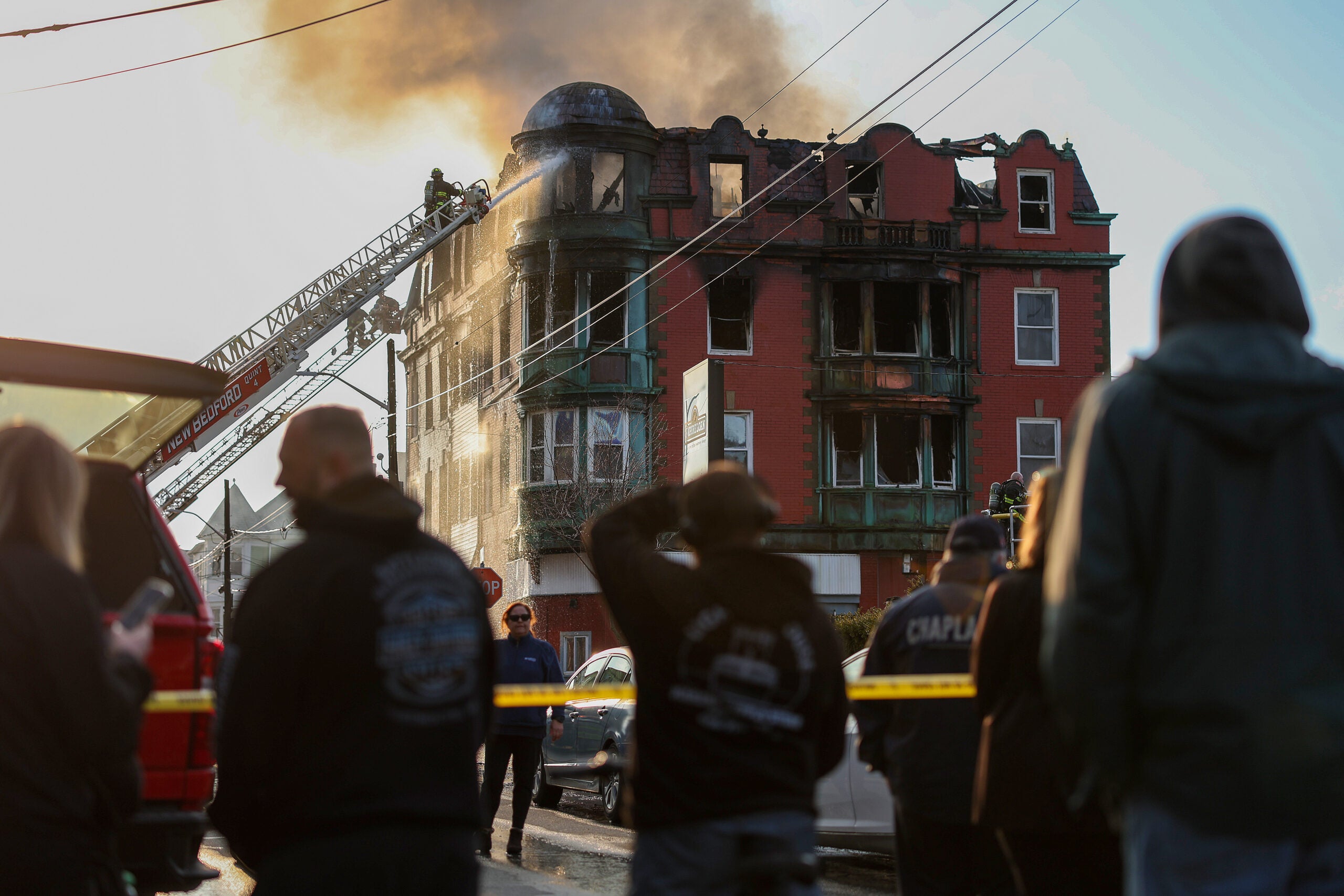 Several people look at the Royal Crown Lodging, a New Bedford rooming house that erupted in flames.