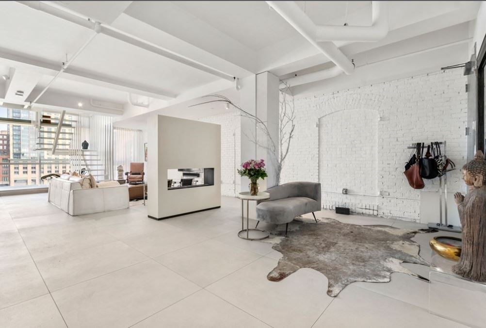 An open room with exposed beams and ductwork, white walls, and a tile floor. There's a double-sided fireplace and a animal-skin rug.