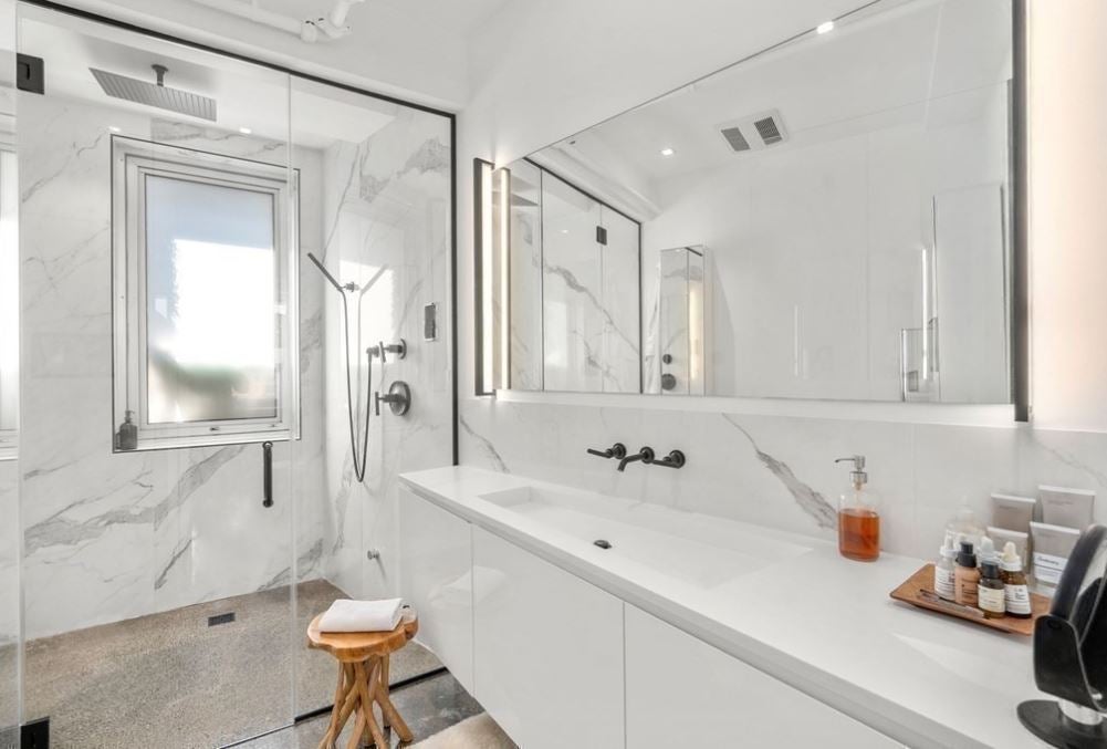 A two-sink vanity with white cabinetry, and a walk-in shower with a window.