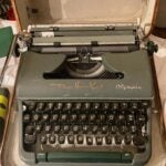 A dark green vintage Olympia typewriter in its wooden carrying case. Tom Hanks has autographed above the keyboard in a bronze marker.