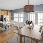 A view into a kitchen/dining area in an East Boston home with a wooden table, a copper drum shade light, wood cabinetry, and a metal island with seating for two.