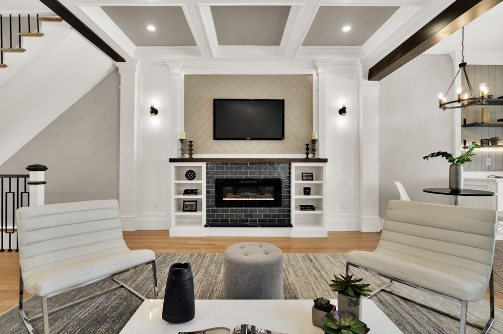a room with gray walls, a coffered ceiling, white trim, and a black brick mantel flanked by built-in shelving.