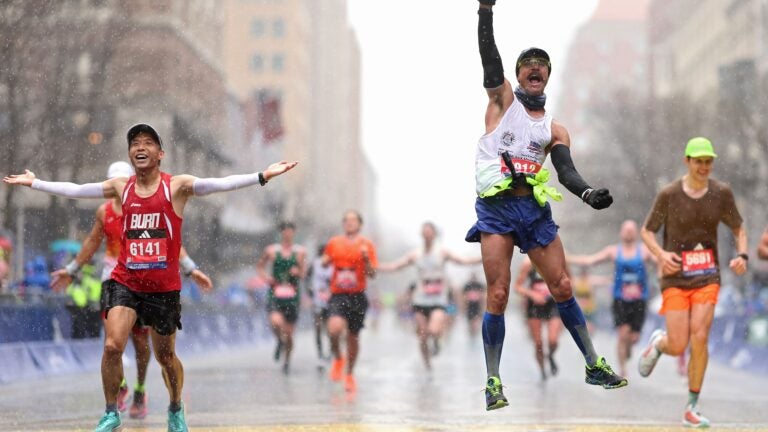 Fernando Ferreira celebrates in the rain as he crosses the finish line next to Zhenfei Lu, left, during the 127th Boston Marathon on Monday.