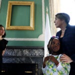 Governor Healey places her hands on the shoulders of six-year-old Emanuela Njinyah in front of the empty frame