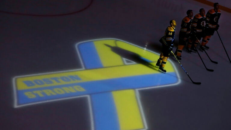 Boston Bruins hockey starters, including defenseman Dennis Seidenberg (44), stand next to a ribbon projected onto the ice at TD Garden in Boston, Wednesday, April 17, 2013, during a pregame ceremony in the aftermath of Monday's Boston Marathon bombings.