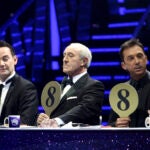 Three judges in tuxedoes sit behind a judges pane;