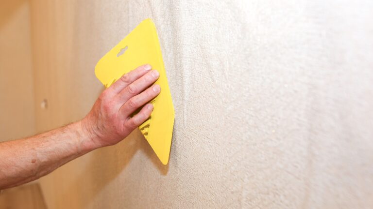 a person tries to smooth out a wallpaper bubble as an illustration for the ask the remodeler column