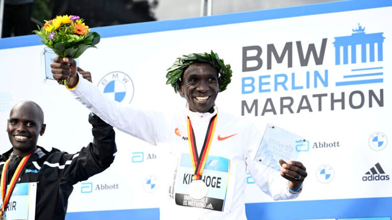 Second placed Kenya's Mark Korir (L) and winner Kenya's Eliud Kipchoge celebrate on the podium after the Berlin Marathon race on September 25, 2022 in Berlin. - Kipchoge has beaten his own world record by 30 seconds, running 2:01:09 at the Berlin Marathon.